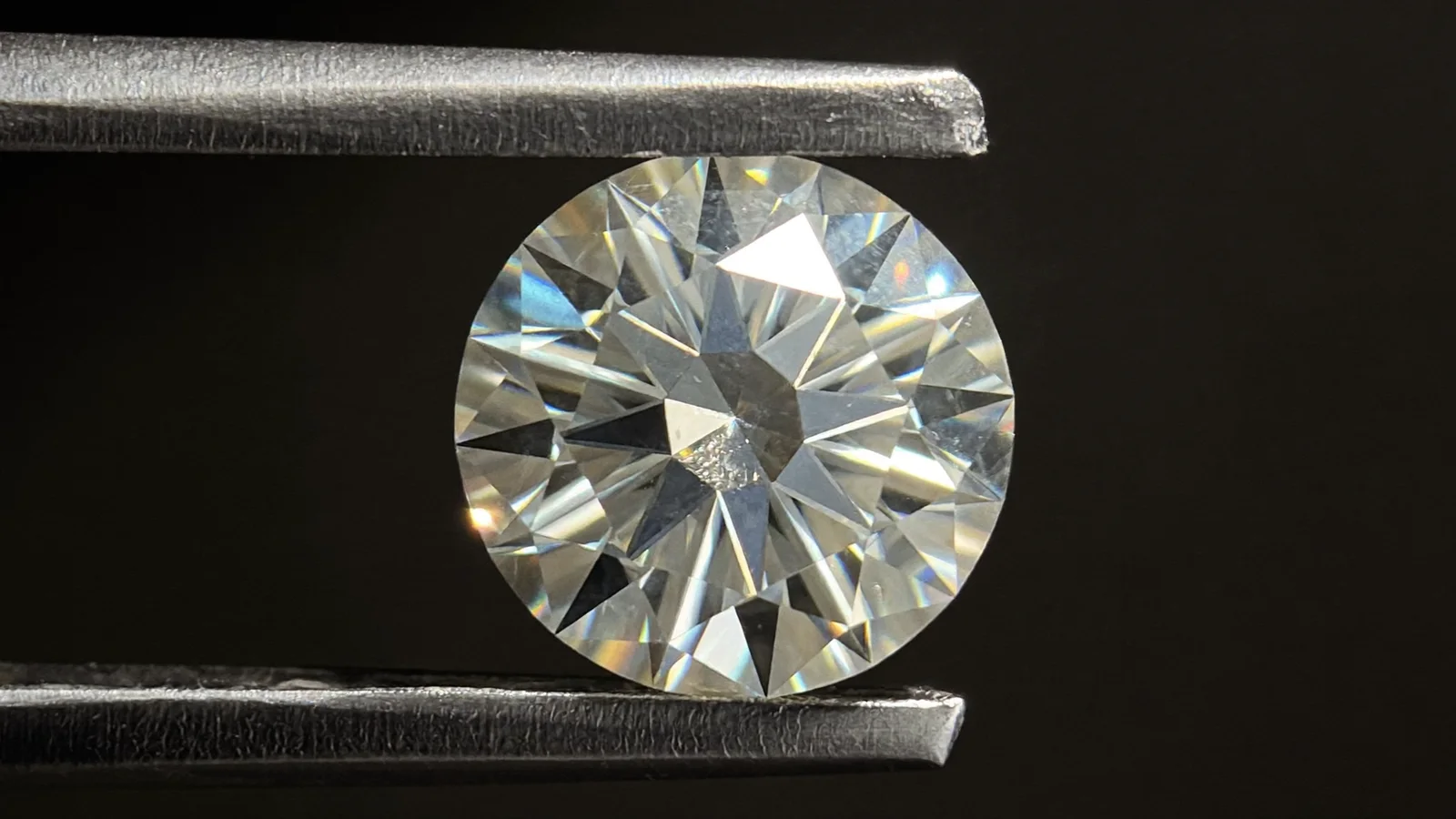 A round brilliant diamond held in tweezers under a raking light